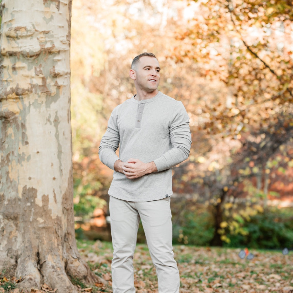 Man wearing a white Henley next to a tree