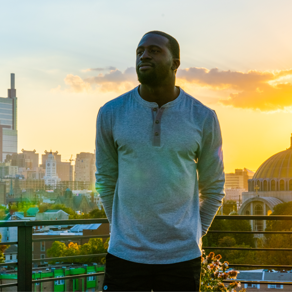 Man wearing a gray Henley in front of a city during a sunset